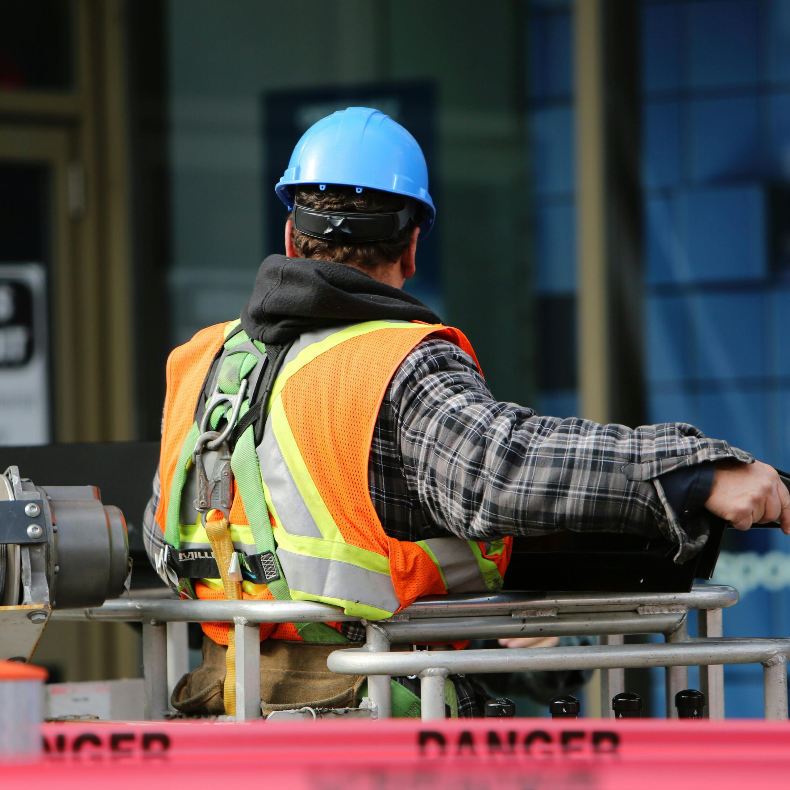 A construction worker wearing a blue helmet and safety vest operates equipment at an urban construction site.